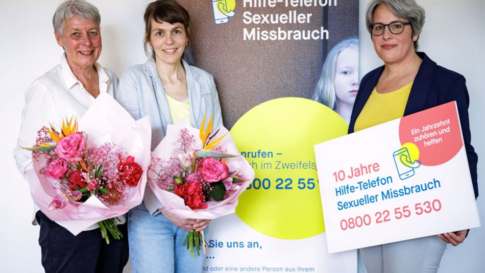 Ein Gruppenfoto mit Silke Noack, Tanja von Bodelschwingh, Kerstin Claus vor einem Aufsteller "10 Jahre Hilfe-Telefon Sexueller Missbrauch".